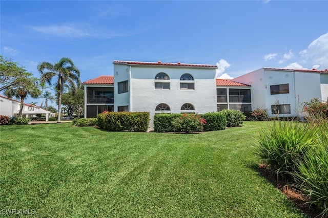 rear view of house with a yard, stucco siding, and a sunroom