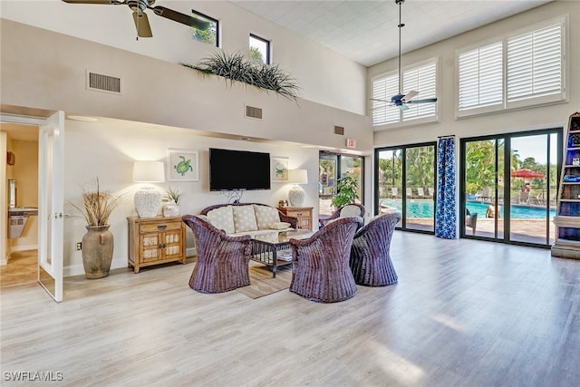 living room with ceiling fan, wood finished floors, a towering ceiling, and baseboards