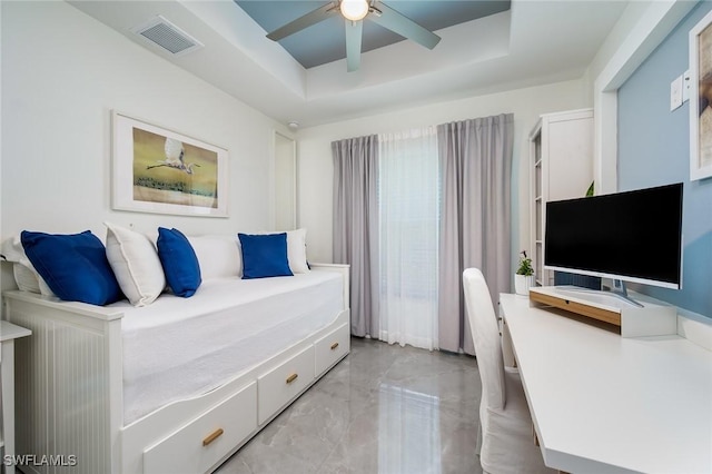 bedroom featuring a tray ceiling, a ceiling fan, light marble finish floors, and a desk