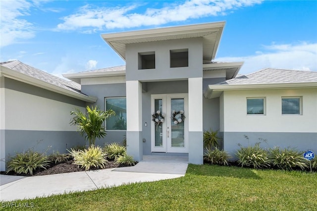 doorway to property with french doors, stucco siding, a yard, and roof with shingles