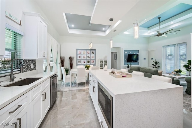 kitchen with a sink, built in microwave, dishwasher, a raised ceiling, and a high ceiling