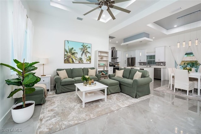 living room featuring ceiling fan, light marble finish flooring, a tray ceiling, recessed lighting, and a towering ceiling