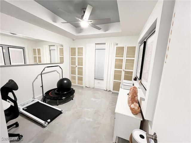 exercise area featuring ceiling fan and a tray ceiling