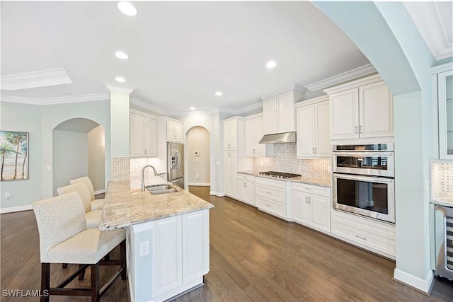 2745 Tiburon Blvd E Unit 102, Naples, FL 34109 - kitchen with stainless steel appliances, under cabinet range hood, a breakfast bar, white cabinetry, and ornamental molding