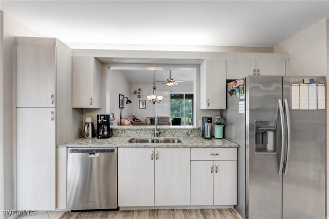kitchen with appliances with stainless steel finishes, a sink, light stone countertops, ceiling fan, and a chandelier