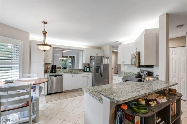 kitchen with appliances with stainless steel finishes, a sink, a peninsula, pendant lighting, and white cabinetry
