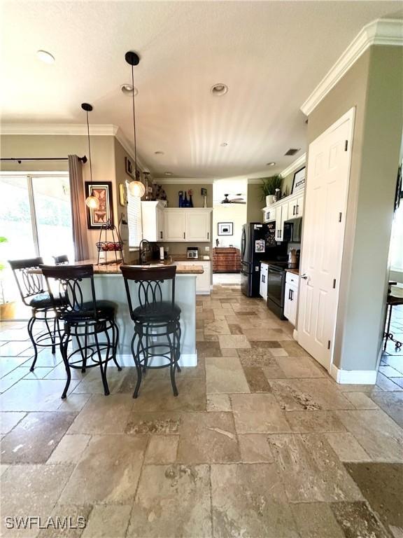 kitchen with stone tile floors, black appliances, ornamental molding, a breakfast bar area, and a peninsula