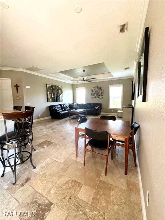 dining area featuring ornamental molding, a tray ceiling, stone tile floors, ceiling fan, and baseboards
