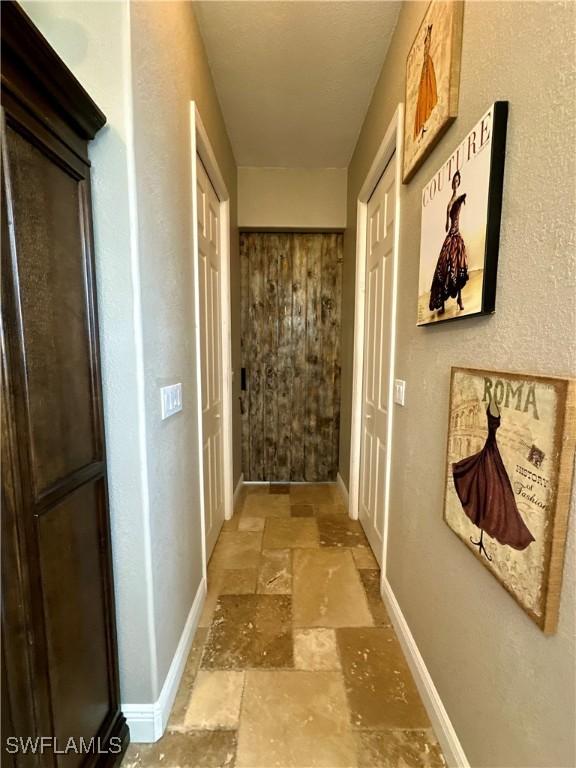 hallway featuring stone tile flooring and baseboards