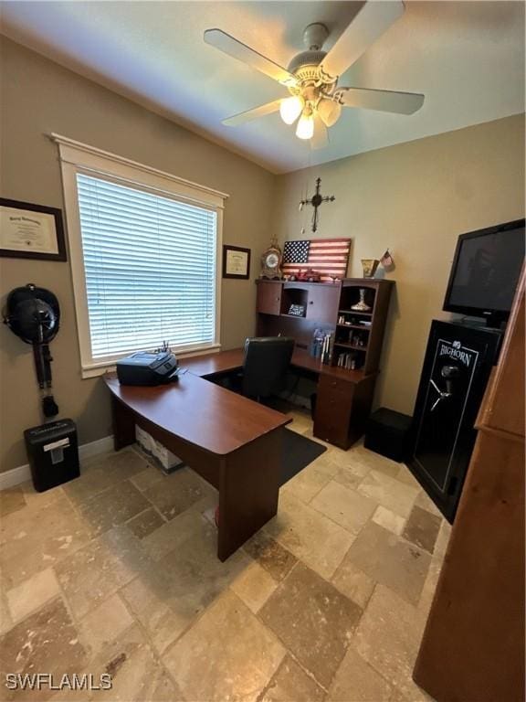 home office featuring stone tile floors, a ceiling fan, and baseboards