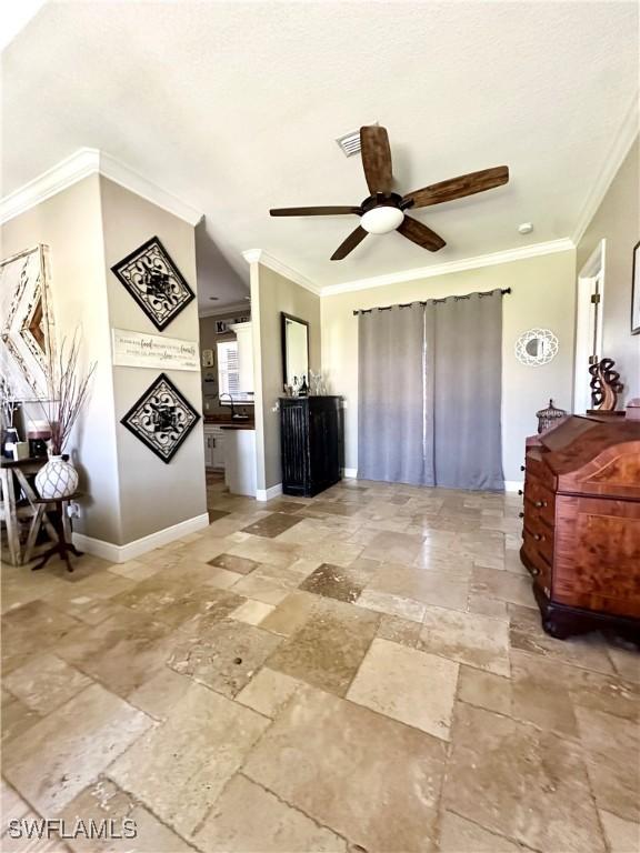 living room with a ceiling fan, stone tile flooring, ornamental molding, and baseboards