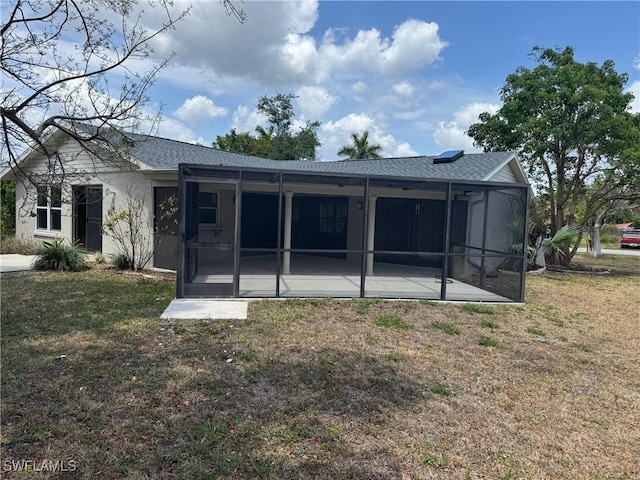 back of property with a lawn, a sunroom, and roof with shingles