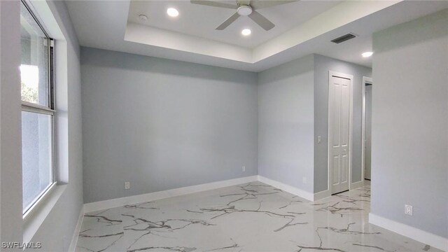 spare room featuring baseboards, recessed lighting, ceiling fan, marble finish flooring, and a raised ceiling