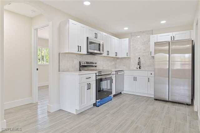 4733/4735 28th St SW, Lehigh Acres, FL 33973 - kitchen with appliances with stainless steel finishes, light countertops, backsplash, white cabinetry, and light wood-type flooring