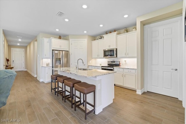 kitchen with stainless steel appliances, a sink, a kitchen breakfast bar, white cabinets, and recessed lighting