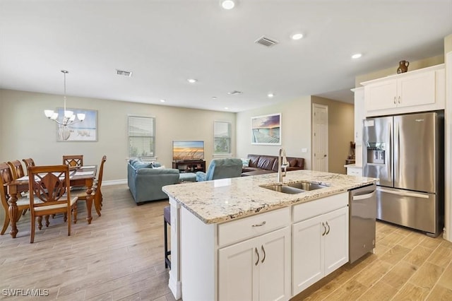 kitchen with stainless steel appliances, a sink, light wood-type flooring, a center island with sink, and light stone counters