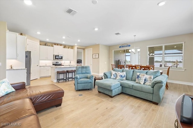 living area featuring light wood-style floors, a chandelier, baseboards, and recessed lighting