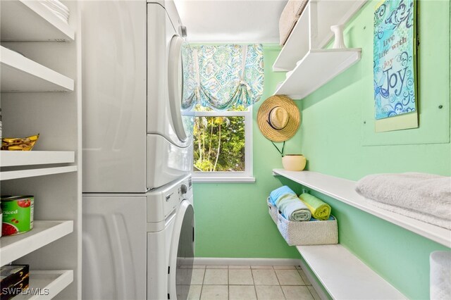 laundry room with stacked washing machine and dryer, baseboards, and light tile patterned flooring