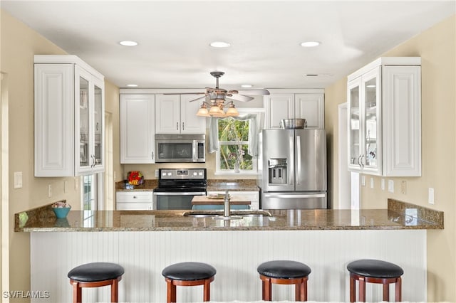 kitchen with appliances with stainless steel finishes, a sink, a peninsula, dark stone countertops, and glass insert cabinets
