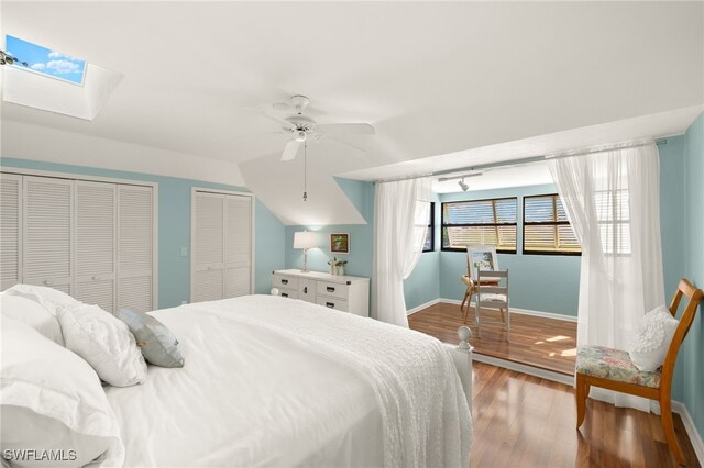 bedroom featuring two closets, baseboards, wood finished floors, a skylight, and a ceiling fan