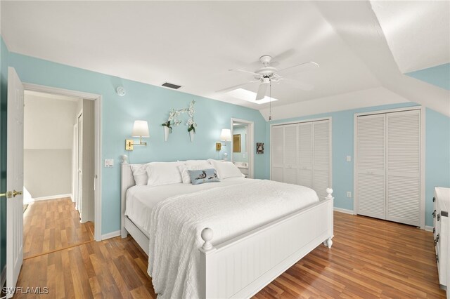 bedroom with two closets, wood finished floors, baseboards, and ceiling fan