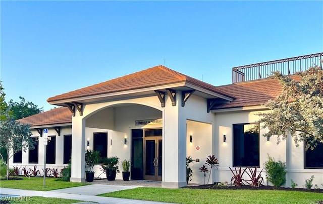 rear view of property featuring a tile roof, stucco siding, and a yard