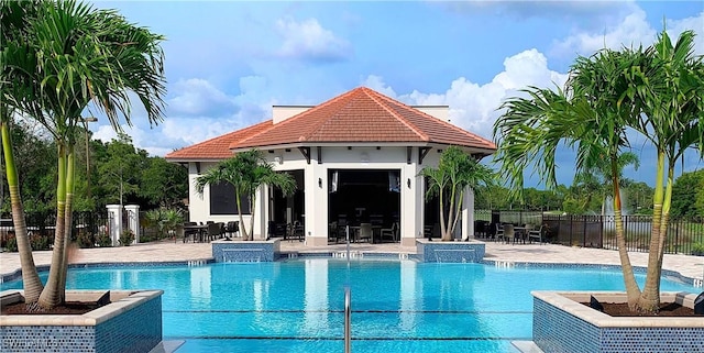 community pool featuring fence, an outdoor structure, an exterior structure, and a patio area
