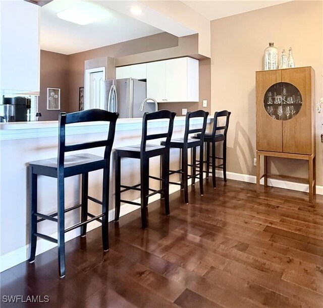 kitchen featuring freestanding refrigerator, white cabinets, a breakfast bar, and a peninsula