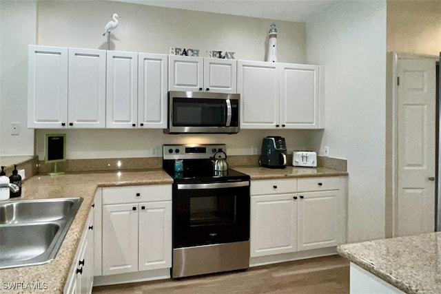 kitchen with appliances with stainless steel finishes, a sink, light wood-type flooring, and white cabinets