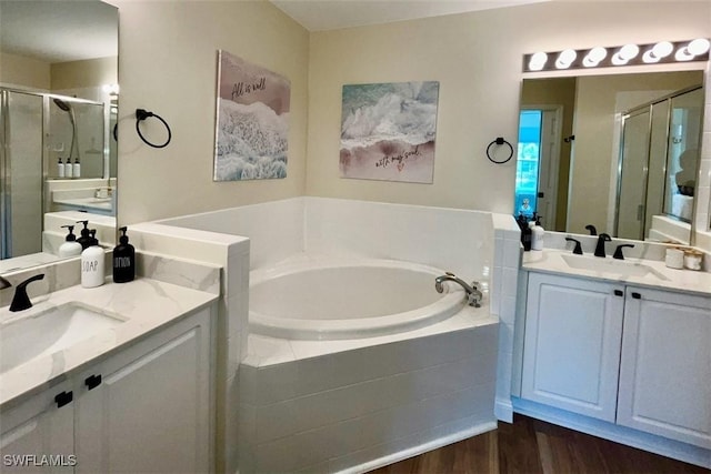bathroom with a stall shower, a garden tub, wood finished floors, and two vanities