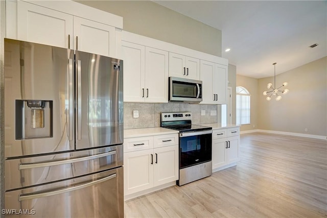 kitchen with appliances with stainless steel finishes, a chandelier, light countertops, light wood finished floors, and baseboards