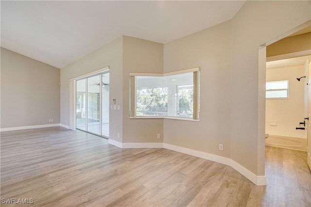 unfurnished room featuring light wood-style flooring, vaulted ceiling, and baseboards