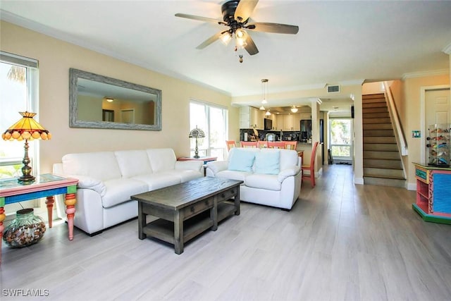 living area featuring crown molding, stairway, light wood finished floors, and a ceiling fan