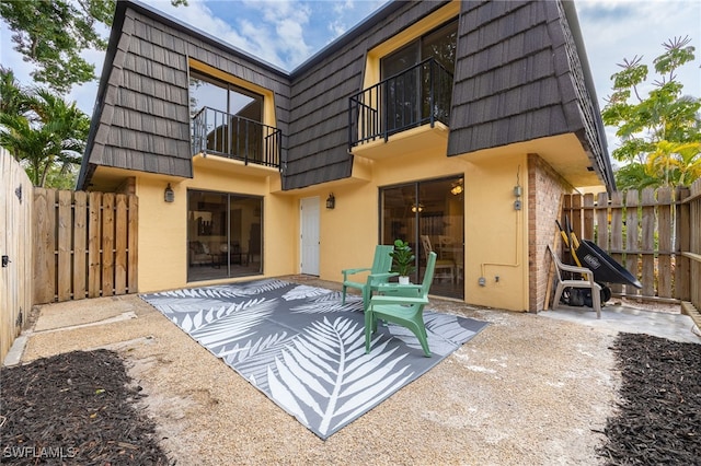 back of property with mansard roof, a balcony, stucco siding, and a patio area