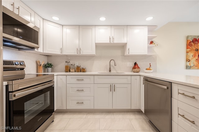 kitchen with stainless steel appliances, a sink, light countertops, white cabinetry, and open shelves