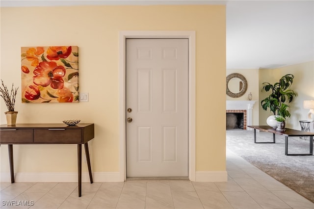 foyer entrance with a brick fireplace, baseboards, light carpet, and light tile patterned floors