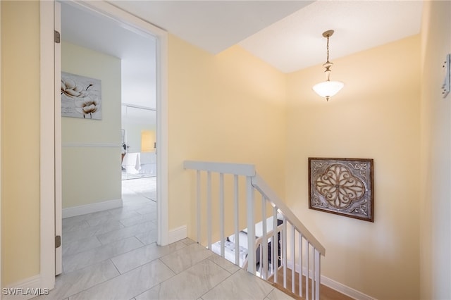 corridor featuring an upstairs landing, tile patterned floors, and baseboards