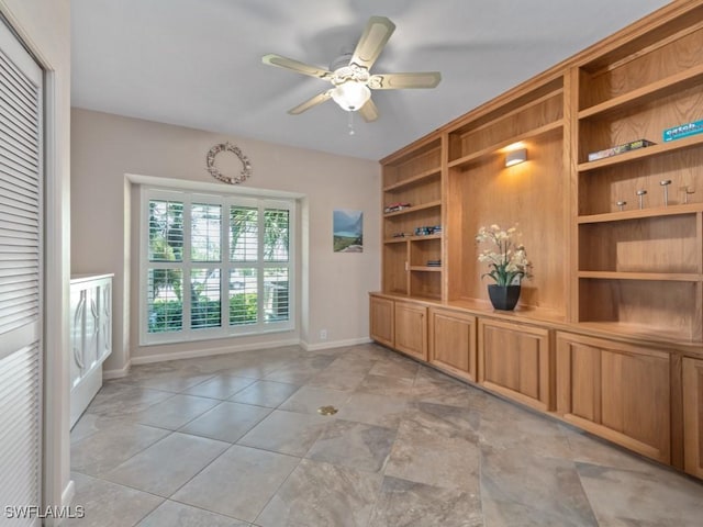 unfurnished dining area featuring baseboards, a ceiling fan, and built in shelves