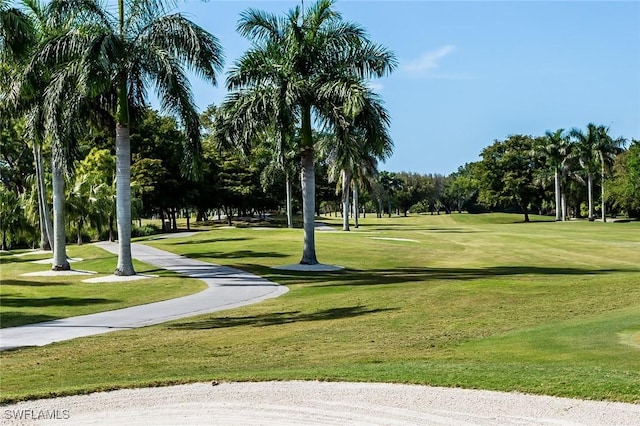 view of property's community featuring a lawn, view of golf course, and view of wooded area