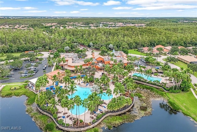 aerial view of property and surrounding area featuring a pool area, a nearby body of water, and a heavily wooded area