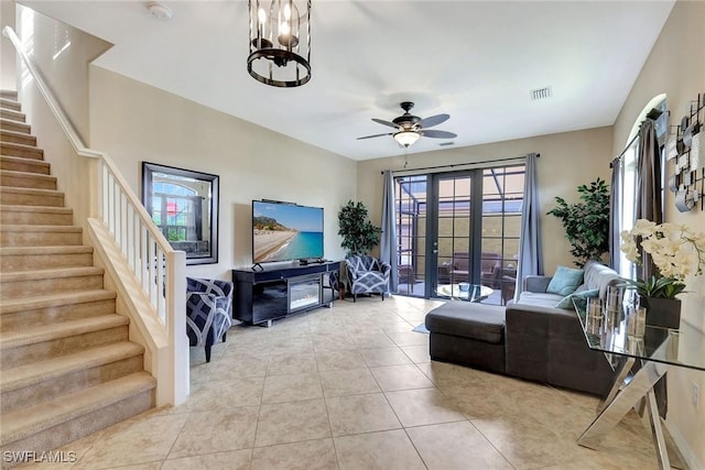 living area with stairs, tile patterned flooring, a ceiling fan, a chandelier, and french doors