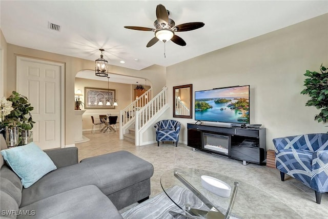 tiled living room featuring stairway, arched walkways, baseboards, ceiling fan, and a chandelier