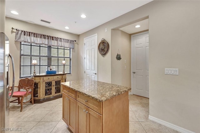 kitchen with light tile patterned floors, light stone counters, a kitchen island, recessed lighting, and freestanding refrigerator