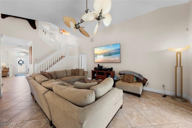 living area featuring stairs, light tile patterned floors, a ceiling fan, arched walkways, and high vaulted ceiling