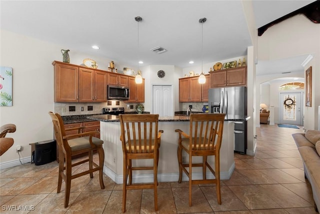 kitchen featuring stainless steel appliances, arched walkways, brown cabinets, a center island, and recessed lighting