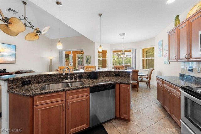 kitchen with appliances with stainless steel finishes, a sink, hanging light fixtures, dark stone countertops, and light tile patterned floors