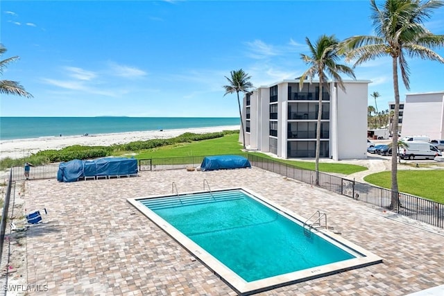 community pool featuring view of water and beach, fence, and a patio area