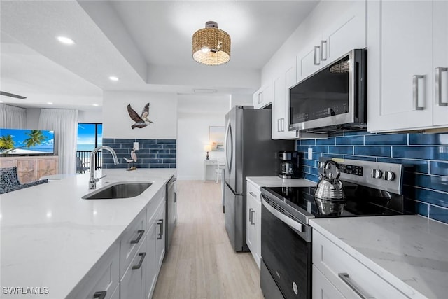 kitchen with stainless steel appliances, a sink, backsplash, light wood-style flooring, and light stone counters