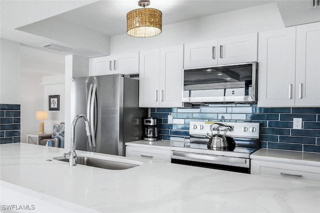 kitchen featuring stainless steel appliances, a sink, white cabinetry, tasteful backsplash, and light stone countertops