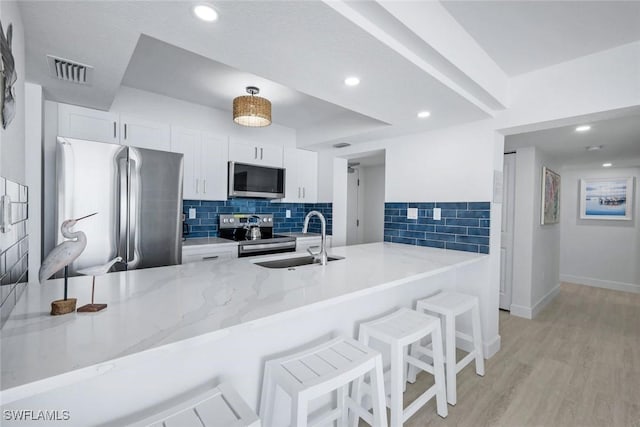 kitchen with stainless steel appliances, a sink, light stone counters, a peninsula, and recessed lighting